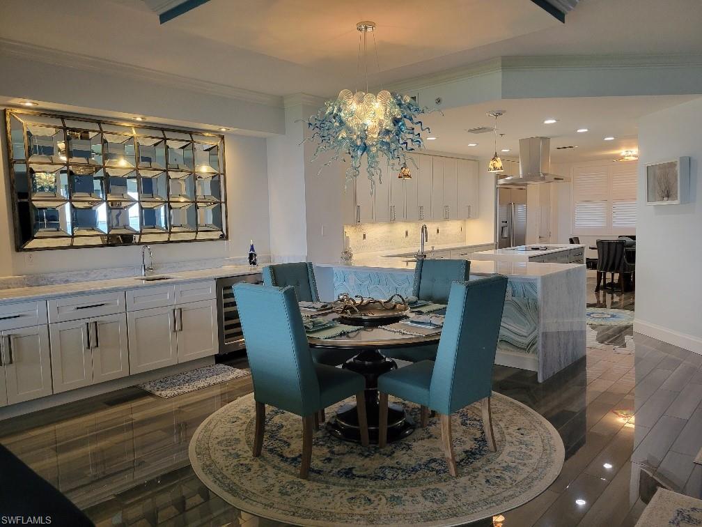 Dining area featuring crown molding, dark wood-style flooring, recessed lighting, beverage cooler, and a chandelier