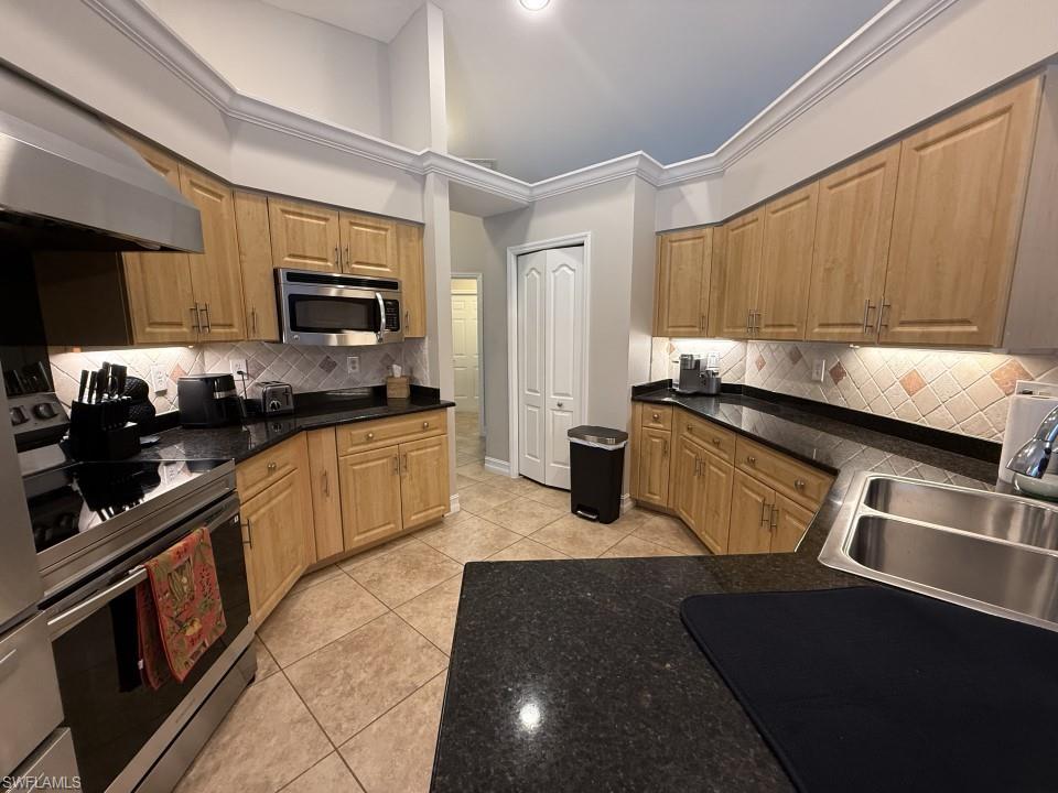 Kitchen with appliances with stainless steel finishes, crown molding, light tile patterned floors, decorative backsplash, and light brown cabinets