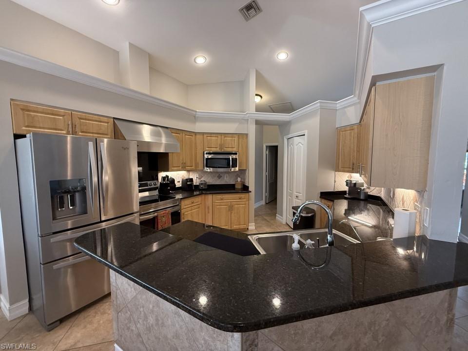 Kitchen featuring stainless steel appliances, light tile patterned floors, a peninsula, wall chimney range hood, and crown molding