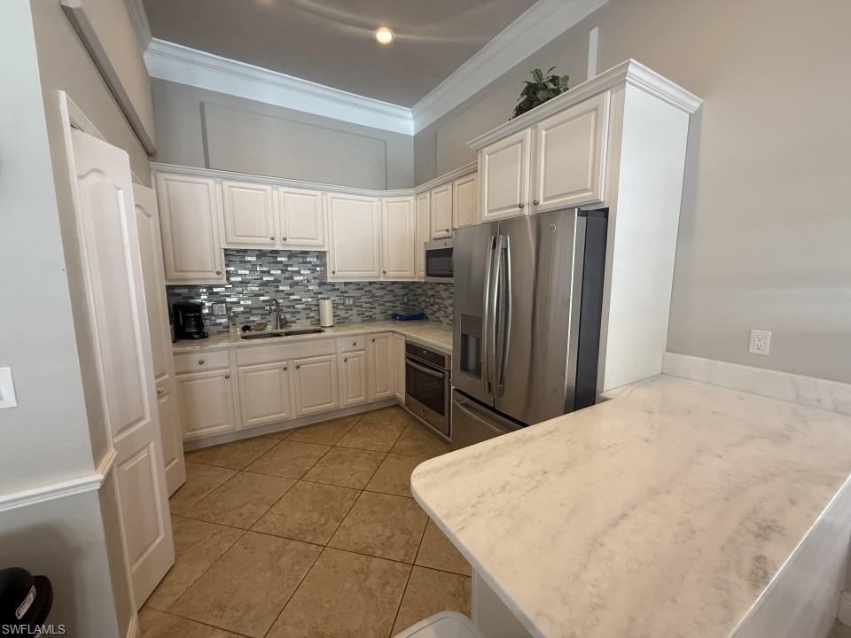Clubhouse Kitchen featuring stainless steel appliances, decorative backsplash, light tile patterned flooring, white cabinets, and light stone countertops
