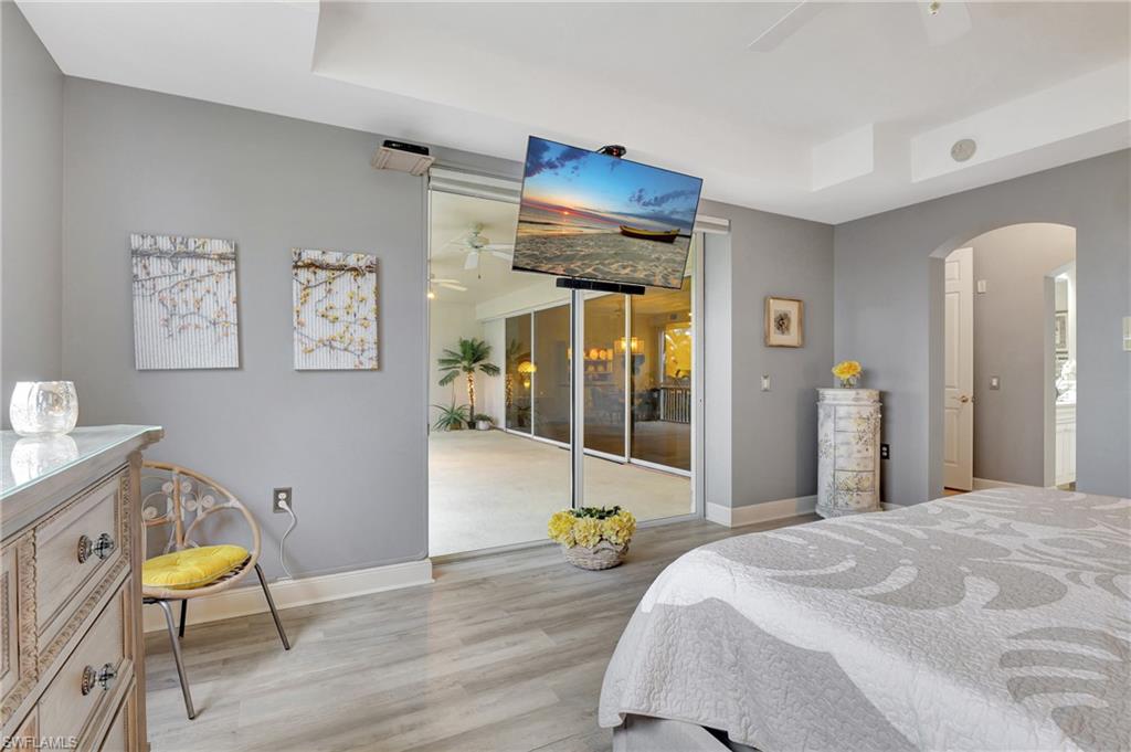 Bedroom featuring light wood-style floors, a raised ceiling, arched walkways, a ceiling fan, and multiple windows
