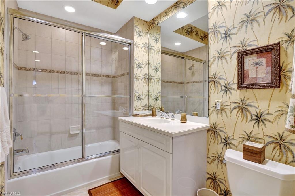 Bathroom with wallpapered walls, bath / shower combo with glass door, vanity, and recessed lighting