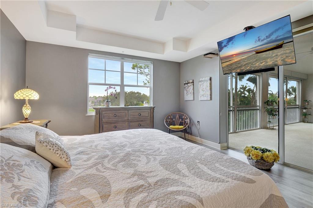 Bedroom with a raised ceiling, multiple windows, light wood-type flooring, and access to exterior