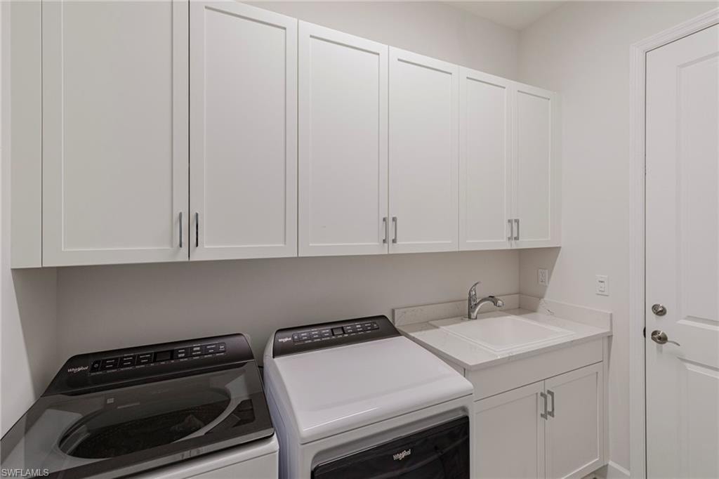 Clothes washing area featuring washing machine and clothes dryer, sink, and cabinets