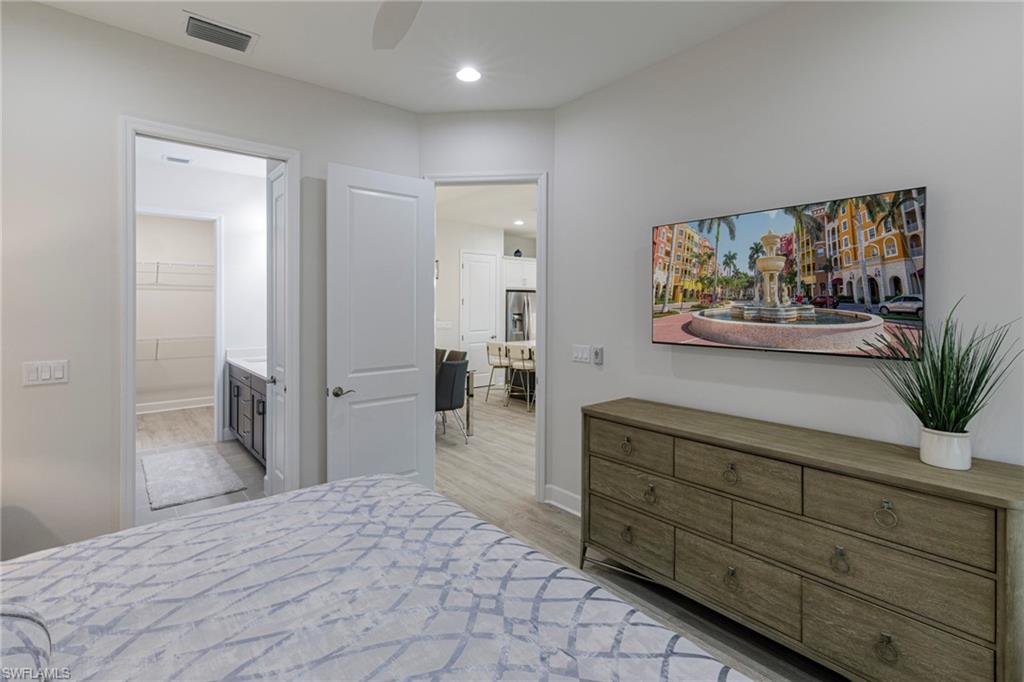 Bedroom with ensuite bathroom, ceiling fan, light wood-type flooring, and a walk in closet