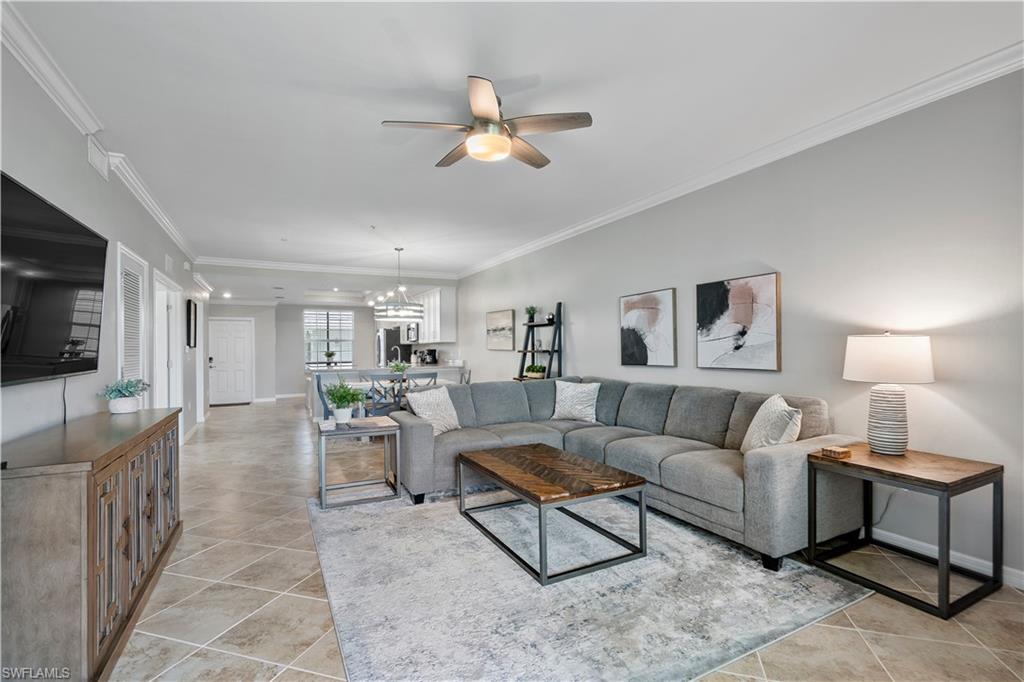Living room with crown molding, a ceiling fan, light tile patterned flooring, and a chandelier