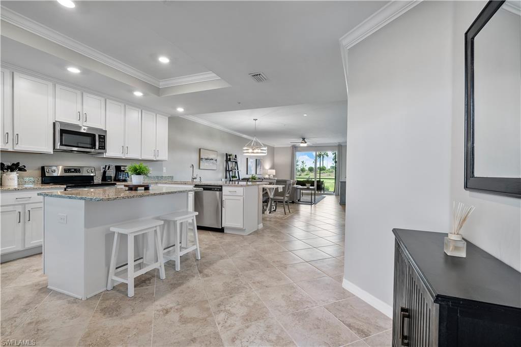 Kitchen featuring decorative light fixtures, a kitchen island, ornamental molding, a breakfast bar, and white cabinets