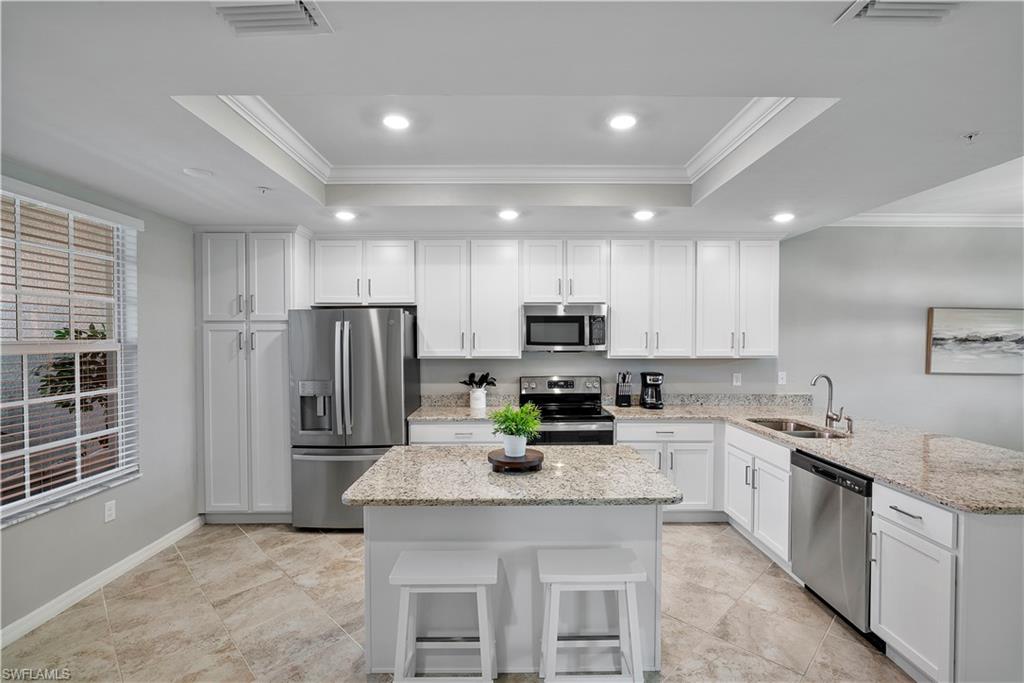 Kitchen featuring white cabinetry, crown molding, appliances with stainless steel finishes, a tray ceiling, and light stone counters