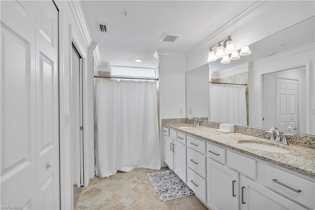 Bathroom featuring a closet, double vanity, a shower with curtain, crown molding, and light tile patterned floors