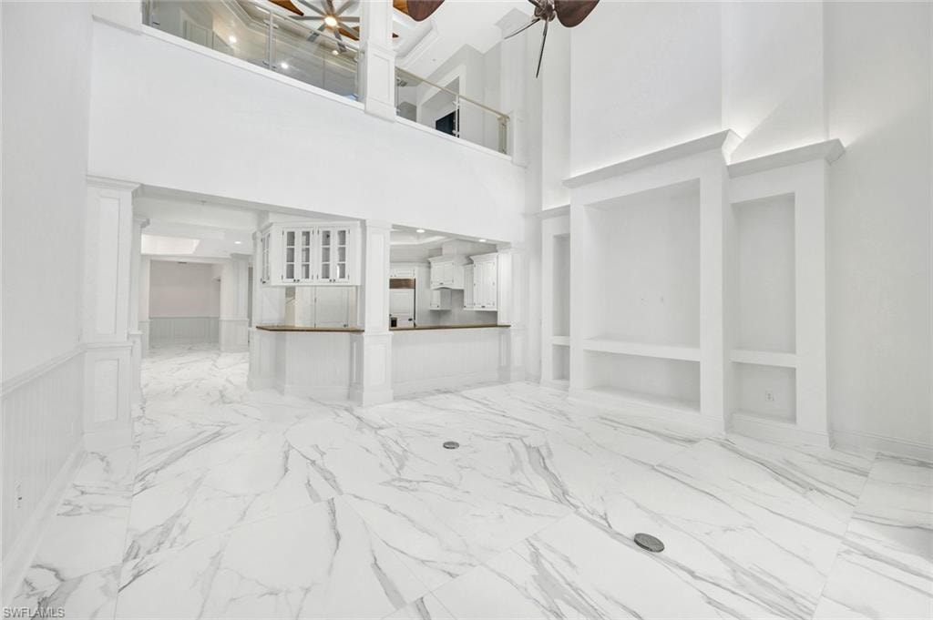 Family-room with light marble finish flooring, a ceiling fan and high ceilings.