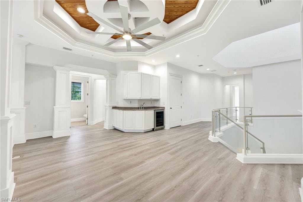 Upstairs sitting area with coffered ceiling, light wood-style flooring, beam ceiling, a tray ceiling and wet-bar.