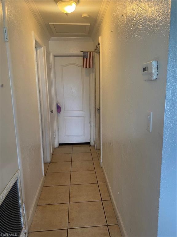 Hallway with light tile patterned flooring, a textured wall, crown molding, and attic access