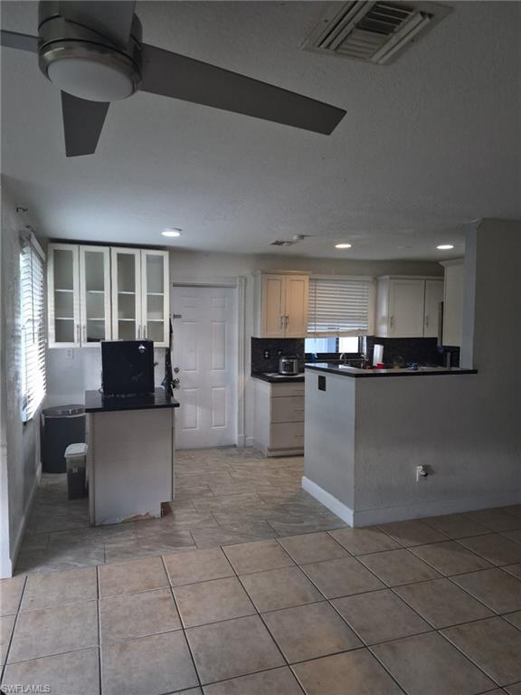Kitchen with a peninsula, dark countertops, backsplash, glass insert cabinets, and light tile patterned floors