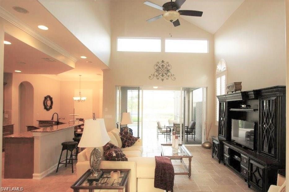 Living room with arched walkways, high vaulted ceiling, healthy amount of natural light, ceiling fan, and a chandelier