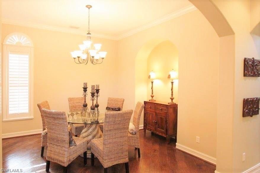 Dining room with ornamental molding, arched walkways, dark wood-type flooring, and a chandelier