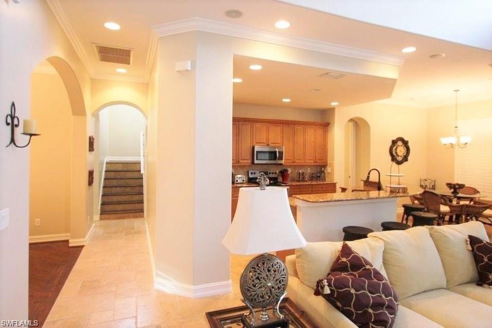 Living room featuring arched walkways, crown molding, recessed lighting, stairway, and a chandelier