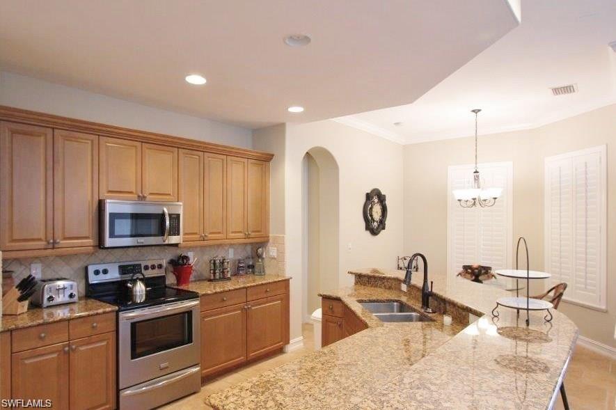 Kitchen with stainless steel appliances, backsplash, a center island with sink, light stone countertops, and pendant lighting
