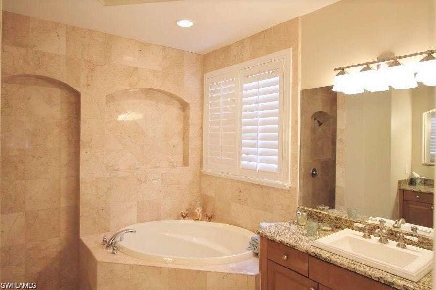 Full bathroom featuring vanity, a garden tub, tile walls, a tile shower, and recessed lighting