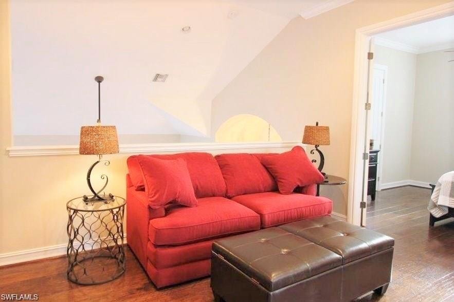 Living area with dark wood-type flooring, crown molding, and lofted ceiling
