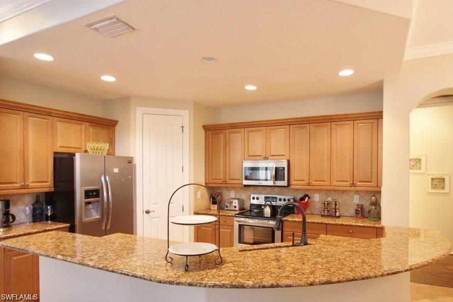 Kitchen featuring appliances with stainless steel finishes, tasteful backsplash, light stone countertops, recessed lighting, and light brown cabinets