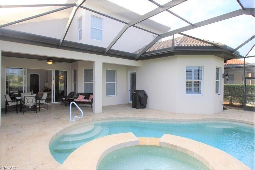 View of pool featuring a sunroom, a patio, a pool with connected hot tub, area for grilling, and glass enclosure