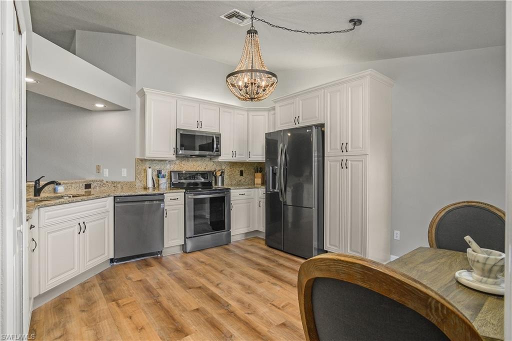 Kitchen featuring stainless steel appliances, white cabinetry, decorative backsplash, light wood-style flooring, and light stone counters