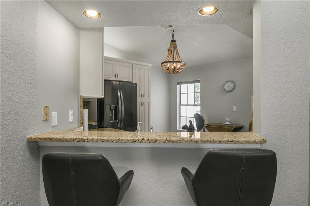 Kitchen featuring a textured wall, a textured ceiling, light stone counters, stainless steel refrigerator with ice dispenser, and pendant lighting
