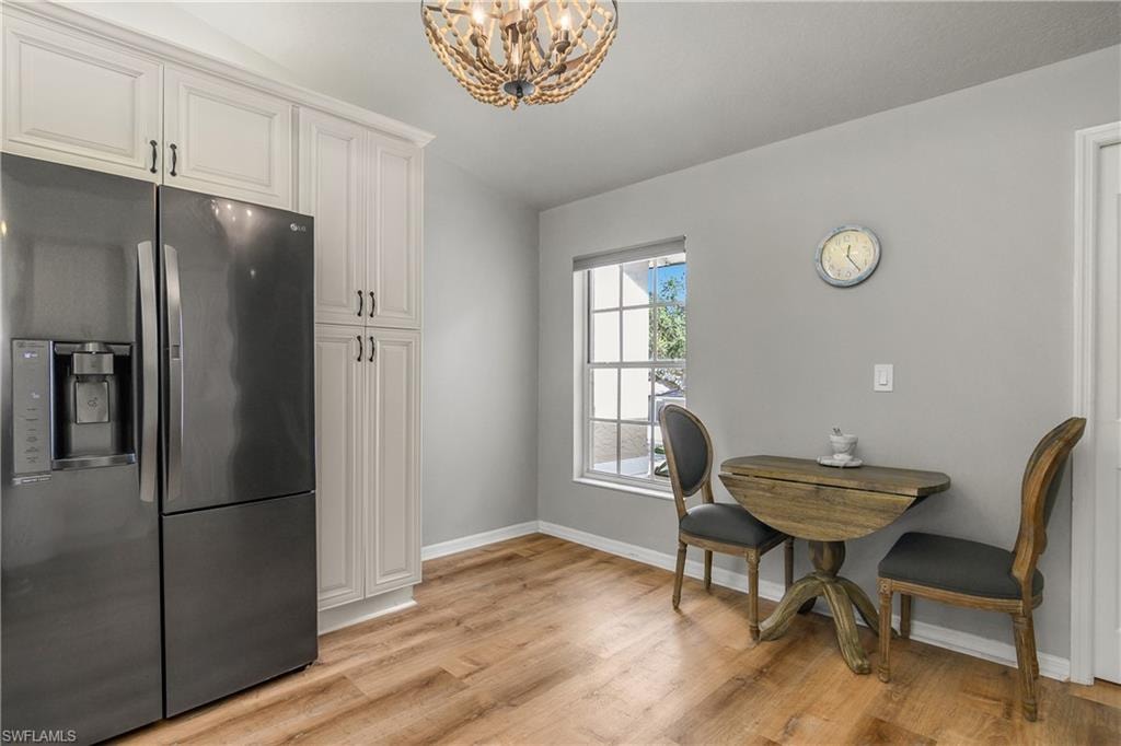 Kitchen featuring stainless steel fridge, light wood-style flooring, a chandelier, white cabinetry, and decorative light fixtures