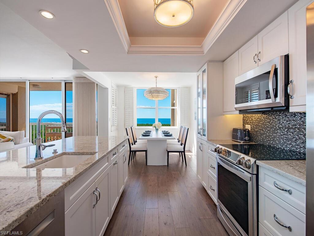 Kitchen with stainless steel appliances, a tray ceiling, white cabinets, light stone countertops, and hanging light fixtures
