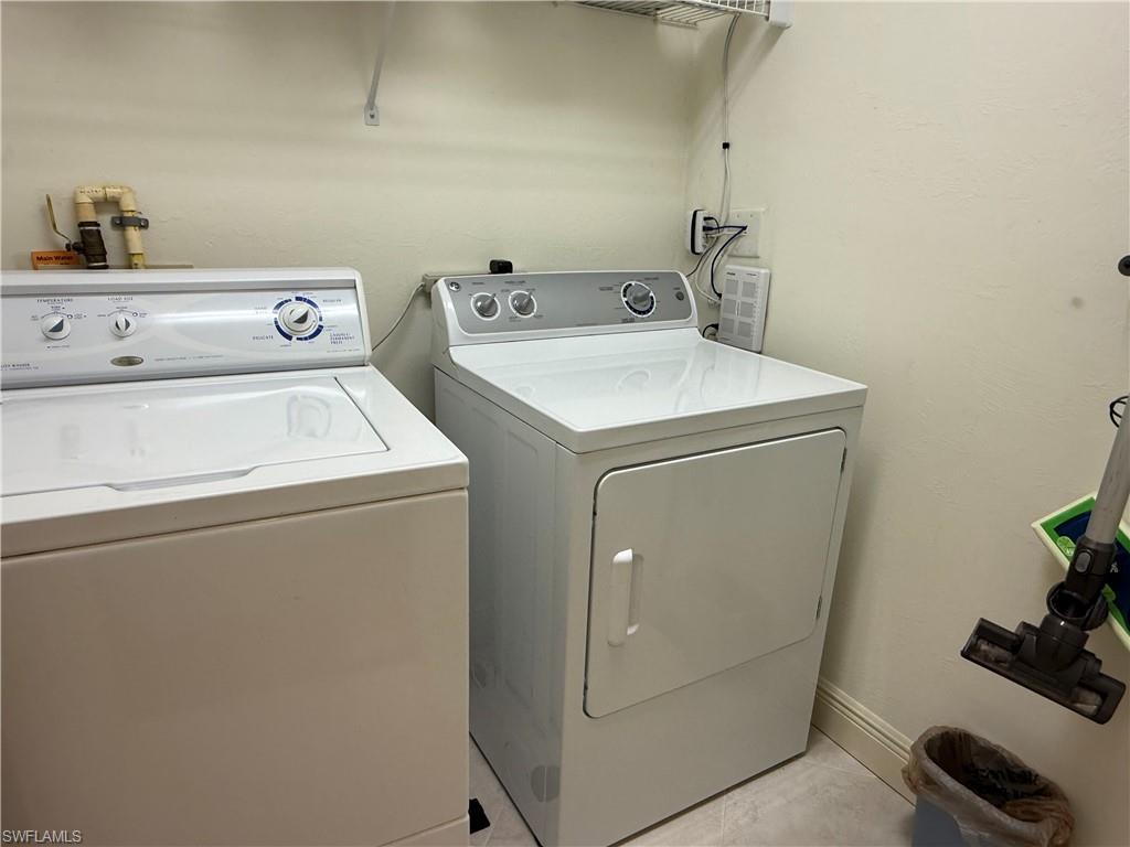 Washroom with washing machine and dryer, light tile patterned floors, and a textured wall