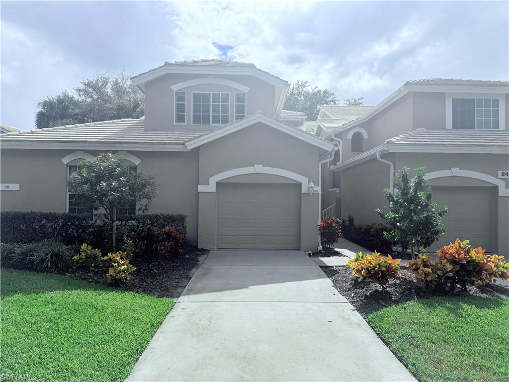 Traditional-style house with driveway, a garage, stucco siding, a front lawn, and a tile roof