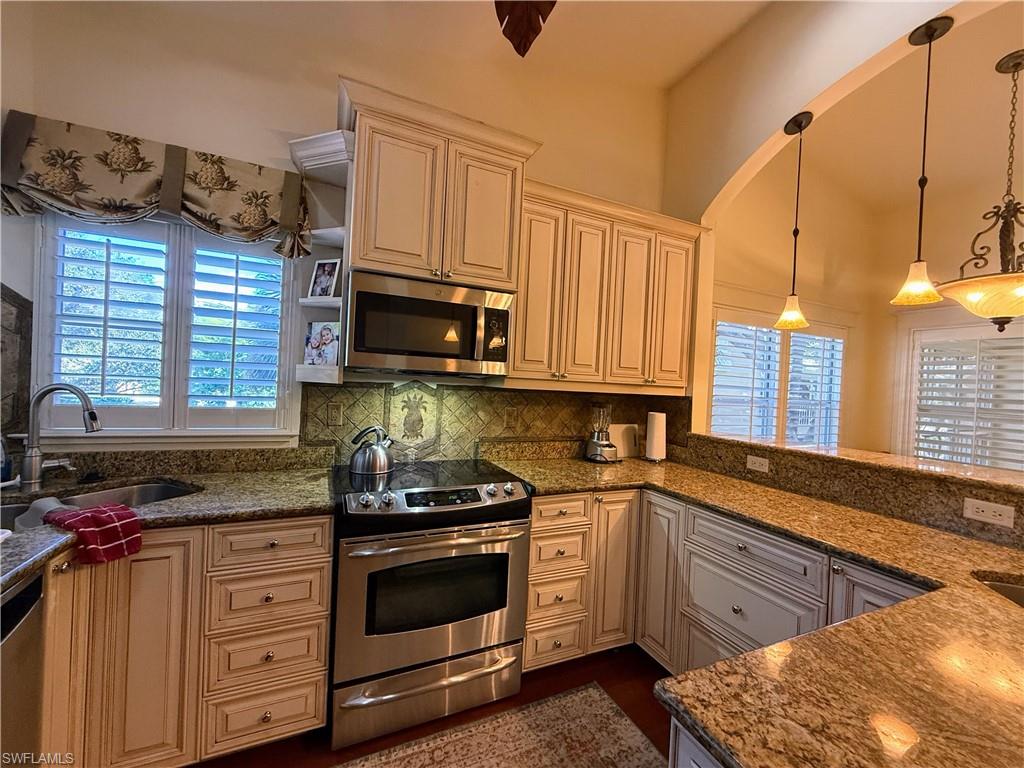 Kitchen with stainless steel appliances, pendant lighting, dark stone countertops, backsplash, and cream cabinetry