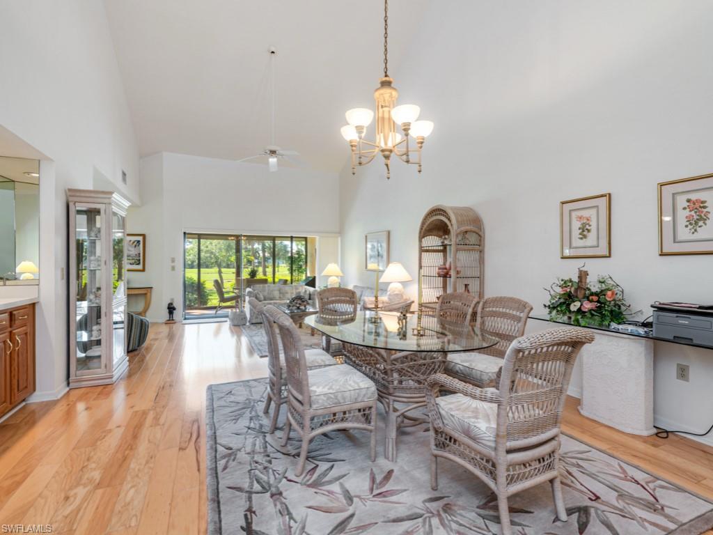 Dining area with high vaulted ceiling, light wood finished floors, a chandelier, and ceiling fan