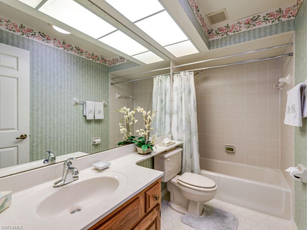 Full bathroom with wallpapered walls, vanity, shower / bath combo with shower curtain, and light tile patterned floors