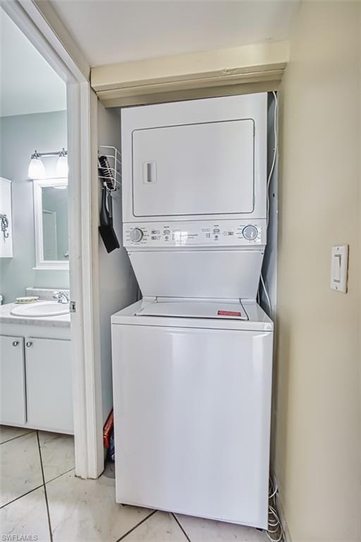 Washroom with stacked washer / drying machine and light tile patterned floors