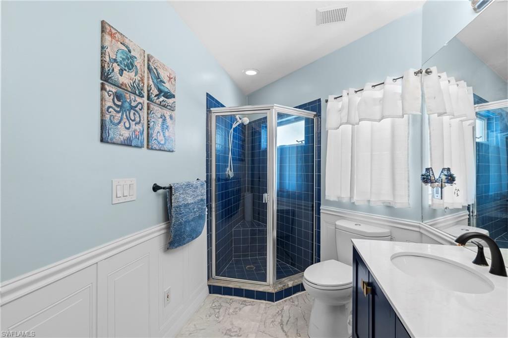 Full bath featuring vanity, a wainscoted wall, a stall shower, light marble finish floors, and a decorative wall