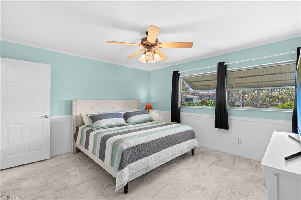 Bedroom featuring wainscoting, light marble finish flooring, ceiling fan, ornamental molding, and a decorative wall