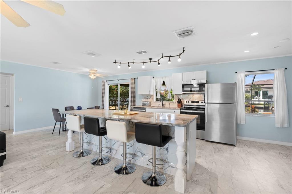 Kitchen with appliances with stainless steel finishes, light stone countertops, a kitchen island, white cabinets, and a breakfast bar