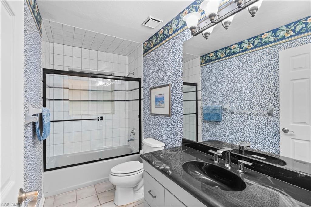 Full bath with combined bath / shower with glass door, light tile patterned floors, vanity, and wallpapered walls