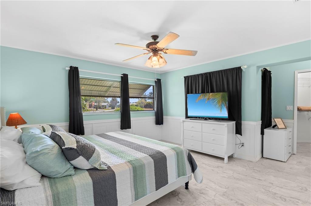 Bedroom featuring wainscoting, marble look tile flooring, crown molding, ceiling fan, and a decorative wall