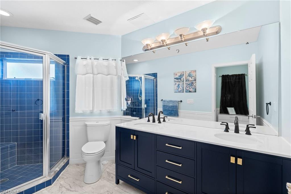 Bathroom featuring double vanity, a shower stall, light marble finish floors, and wainscoting