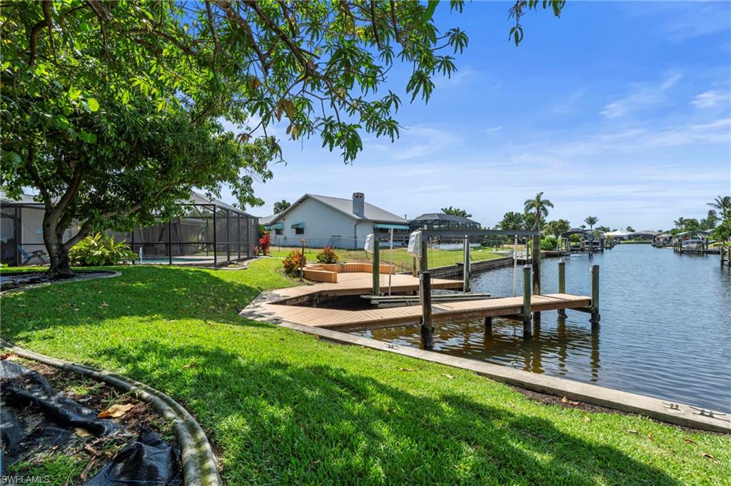 Dock area with a yard, glass enclosure, boat lift, and a water view