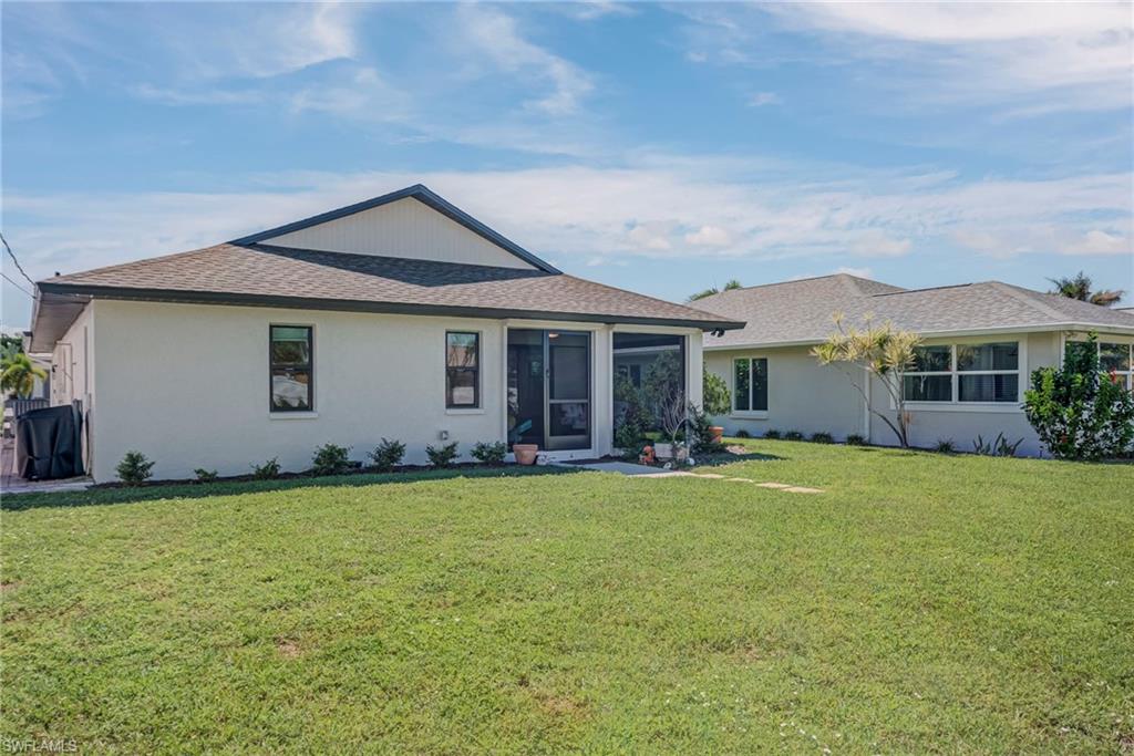 Back of property with a yard, stucco siding, and roof with shingles