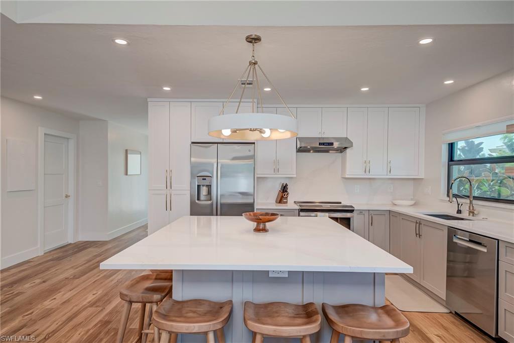 Kitchen with stainless steel appliances, recessed lighting, decorative light fixtures, light wood-type flooring, and a kitchen island
