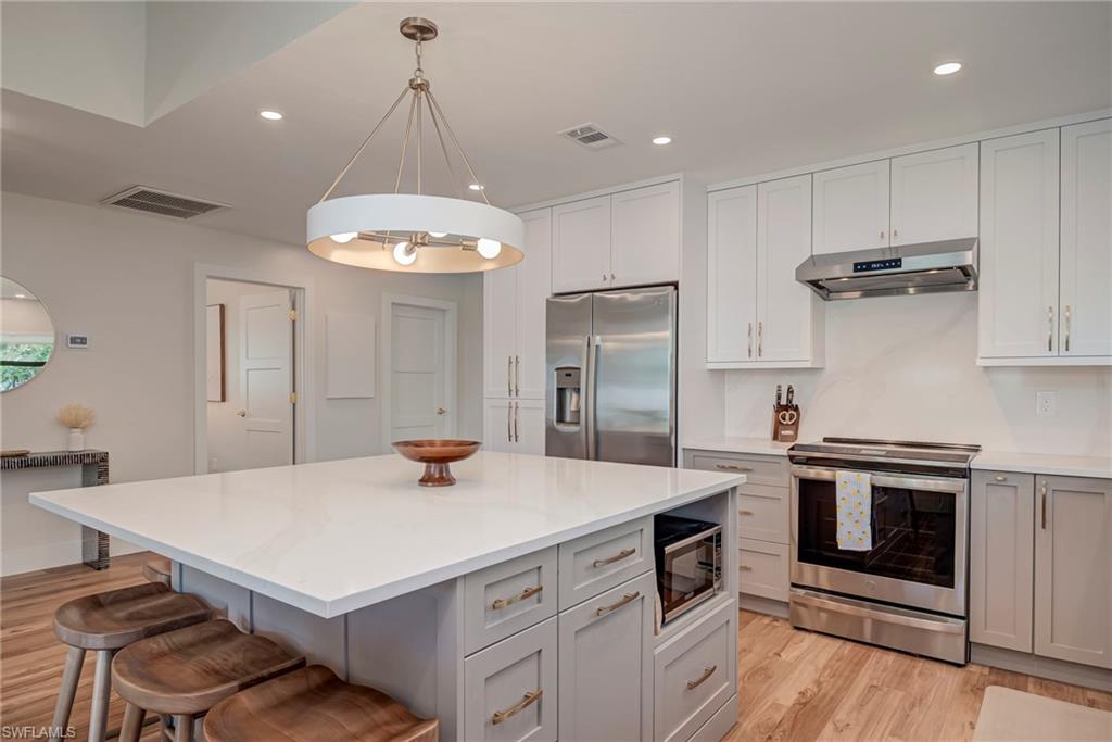 Kitchen with gray cabinets, stainless steel appliances, recessed lighting, white cabinets, and a kitchen bar