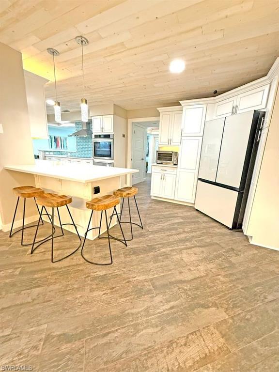 Kitchen featuring wood ceiling, a kitchen bar, hanging light fixtures, freestanding refrigerator, and white cabinets