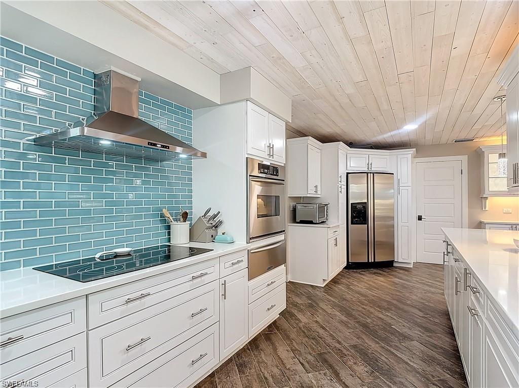 Kitchen featuring white cabinets, wall chimney exhaust hood, appliances with stainless steel finishes, dark wood-type flooring, and wooden ceiling