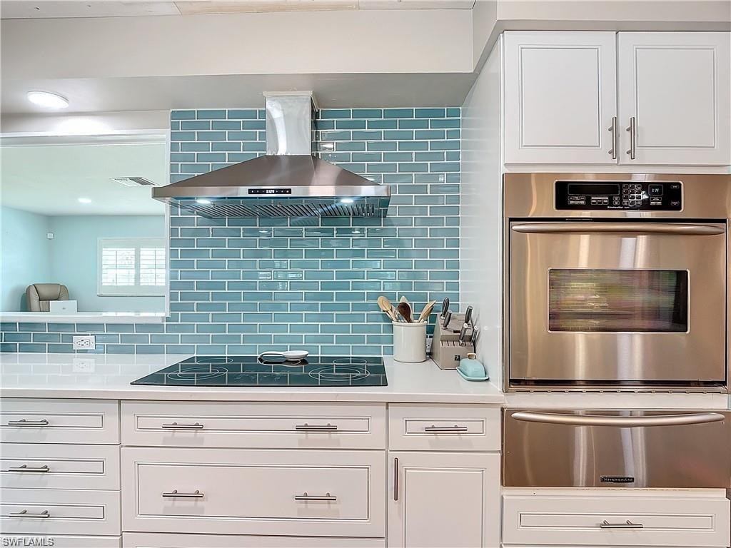 Kitchen featuring white cabinetry, oven, a warming drawer, ventilation hood, and decorative backsplash
