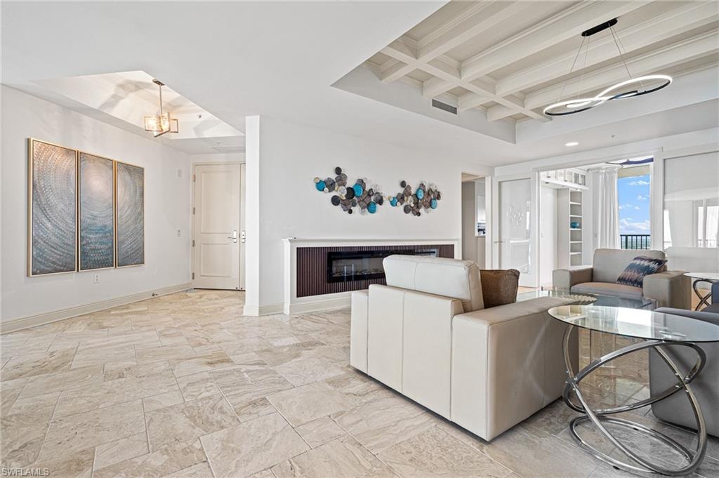 Living room with coffered ceiling, beam ceiling, a chandelier, and a glass covered fireplace