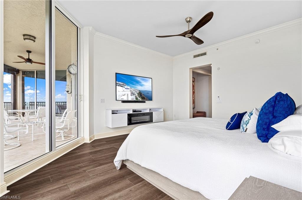 Bedroom with crown molding, ceiling fan, dark wood-type flooring, access to outside, and a glass covered fireplace